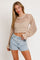 woman wearing a beige crocheted crop top with long bell sleeves and high-waisted denim shorts