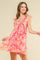 woman wearing a pink floral sundress with ruffled straps and a flared skirt, smiling against a neutral background