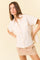 woman wearing a beige short sleeve button-up shirt with two chest pockets and a cream mini skirt
