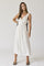woman wearing a white sleeveless maxi dress with a plunging neckline and tie details at the waist