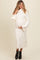 woman wearing a cream long sleeve maternity dress with a cowl neck, holding her baby bump