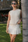 woman wearing a beige sleeveless sweater top paired with a matching mini skirt, standing outdoors by a palm tree