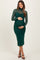 woman wearing a dark green maternity dress with a mesh long sleeve overlay and holding her baby bump