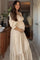 woman wearing a cream floral maternity dress with puff sleeves, holding her baby bump in a sunlit room