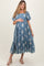 woman wearing a blue floral embroidered maternity dress, holding her baby bump, with puff sleeves and a tiered skirt