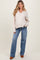 woman wearing a light beige ribbed maternity sweater with a v-neck and blue flared jeans, smiling with long wavy hair