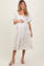 woman wearing a cream maternity dress with bow embroidery and a tiered skirt, holding her baby bump