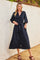 woman wearing a navy blue long sleeve button-up dress with a tie waist detail standing against a textured wall