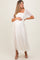woman wearing a white maternity dress with short sheer sleeves and floral detailing, holding her baby bump