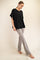 woman wearing a black oversized t-shirt and light gray flared pants, standing barefoot against a neutral background