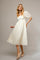 woman wearing a cream mid-length puff sleeve dress with floral embroidery and beige flats