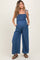 woman wearing a blue striped maternity jumpsuit with a smocked bodice and side pockets, featuring adjustable straps and a baby bump visible
