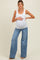 woman wearing a white ribbed maternity tank top and blue wide-leg maternity jeans, posing with her baby bump visible