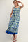 woman wearing a blue and green floral maxi dress with a smocked bodice and pockets, smiling and waving