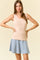 woman wearing a beige ribbed tank top with scalloped edges and a light blue flared skirt
