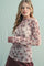 woman wearing a light pink long sleeve top with floral print and ruffled hem, standing against a pale background