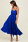 woman wearing a blue pleated maxi dress with spaghetti straps and a cinched waist, styled with strappy sandals