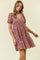 woman wearing a maroon floral short sleeve dress with a v-neck and gathered waist, smiling and posing