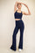 woman wearing a navy blue cropped tank top and flared leggings, posing with one arm raised