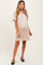 woman wearing a beige maternity polo dress with black trim and holding her baby bump