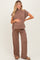 woman wearing a brown striped maternity set with a short sleeve top and wide-leg pants, holding her baby bump