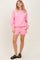 woman wearing a pink oversized sweatshirt and matching shorts with pockets and a drawstring