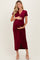 woman wearing a burgundy maternity dress with short sleeves and a gathered front, holding her baby bump