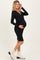 woman wearing a black maternity wrap dress with long sleeves and a tie detail, smiling and holding her baby bump