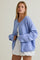 woman wearing a light blue oversized cardigan over a white crop top and white pleated shorts