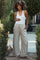 woman wearing a white maternity tank top and light beige wide-leg pants, holding her baby bump outdoors