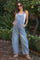 woman wearing a light blue maternity overall with wide legs and a white tank top, standing outdoors with sunglasses on
