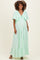woman wearing a mint green maternity maxi dress with flutter sleeves and a tie detail, showing her baby bump