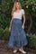 woman wearing a denim tiered maternity skirt with a drawstring waist and a light beige short sleeve top, standing in a garden