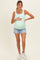 woman wearing a light green maternity tank top and distressed denim shorts, holding her baby bump