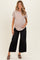 woman wearing a light taupe short sleeve maternity top and black wide-leg jeans, holding her baby bump