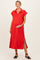 woman wearing a red maternity dress with a collared neckline and side slits, smiling and holding her baby bump