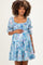woman wearing a light blue floral maternity dress with puff sleeves and tiered ruffles, showcasing her baby bump
