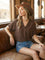 woman wearing a brown v-neck short sleeve top and denim shorts, sitting on a leather couch in a rustic setting