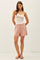 woman wearing a white tank top and pink tailored shorts, standing against a plain background