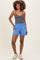 woman wearing a gray tank top and blue maternity shorts, standing with a smile on a light background