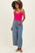 woman wearing a fuchsia maternity tank top and light blue wide-leg maternity pants, holding her baby bump