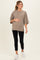 woman wearing a taupe oversized maternity top and black leggings, gently cradling her baby bump