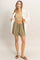 woman wearing a beige cropped tank top, olive green drawstring shorts, and an oversized white button-up shirt