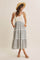 woman wearing a light grey floral maxi dress with spaghetti straps and pockets, accessorized with a straw hat