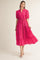 woman wearing a bright pink tiered maxi dress with short puff sleeves and a tie waist detail