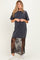 woman wearing a dark gray maternity dress with a sheer black lace overlay and white sneakers, baby bump not visible