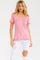 woman wearing a pink short sleeve top with a heart pattern and button details, paired with white ripped jeans