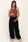 woman wearing a brown maternity tank top and black wide-leg maternity pants, holding her baby bump