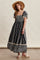 woman wearing a navy blue floral maxi dress with puff sleeves and a tiered skirt, styled with a straw hat and sandals