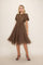woman wearing a brown polka dot dress with puff sleeves and a keyhole neckline, standing against a neutral background
